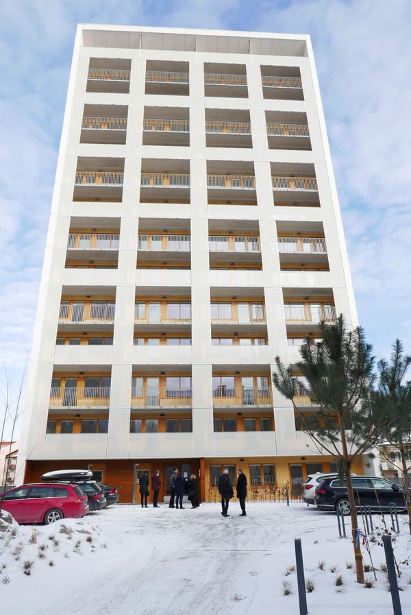 Högt bostadshus med flera balkonger och ett par personer samlade vid entrén i vintermiljö