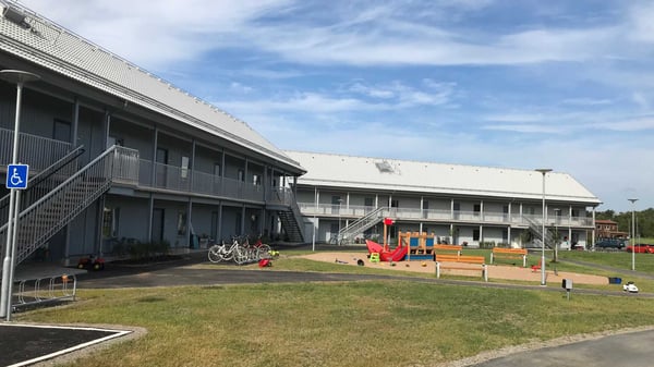 Tvåvånings flerbostadshus med innergård, cyklar och en lekplats under en blå himmel
