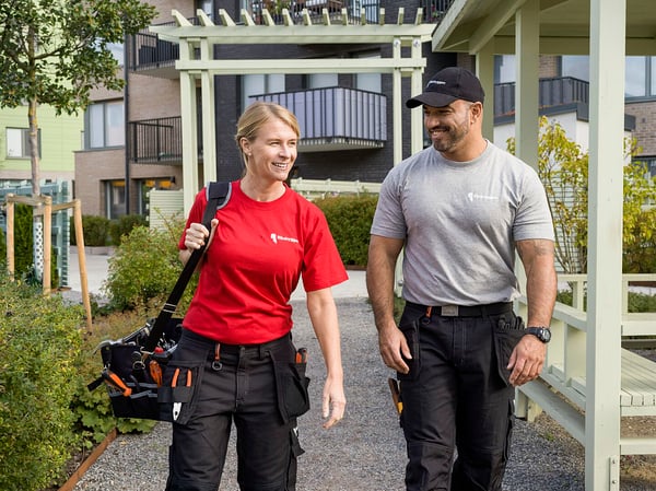 Två personer i Riksbyggen kläder som går på en grön innergård