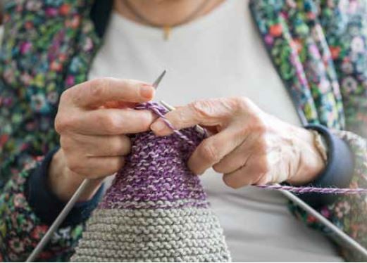 Närbild av en person som stickar med lila och grått garn
