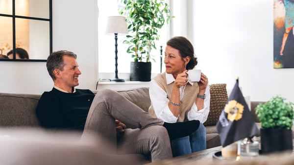 Två personer sitter i en soffa och dricker kaffe i ett ljust vardagsrum