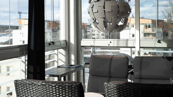 Vardagsrum med stora fönster, svart soffa och utsikt över bostadshus