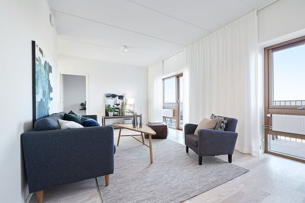 Ljust vardagsrum med mörk soffa, fåtölj, soffbord och stora fönster
