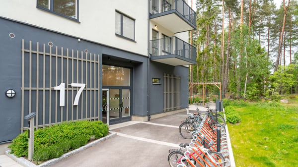 Flerbostadshus med nummer 17, entré och cykelparkering vid grönskande skogsmiljö