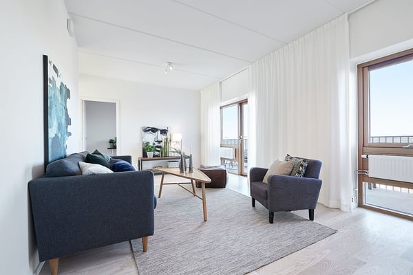 Ljust vardagsrum med mörk soffa, fåtölj, soffbord och stora fönster