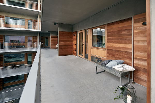Balkong med träpanel, glasdörrar och sittbänk med kuddar