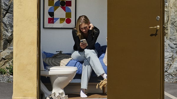 Person som sitter på en säng och använder mobil i ett minihus