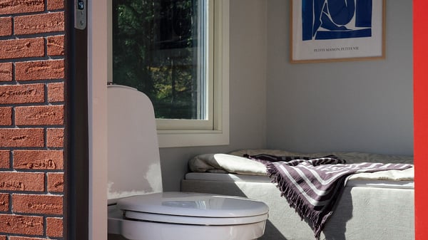 Minihus i tegel med säng, toalettstol och fönster