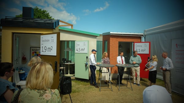 Flera personer samlas utomhus vid små färgglada husmoduler i Almedalen