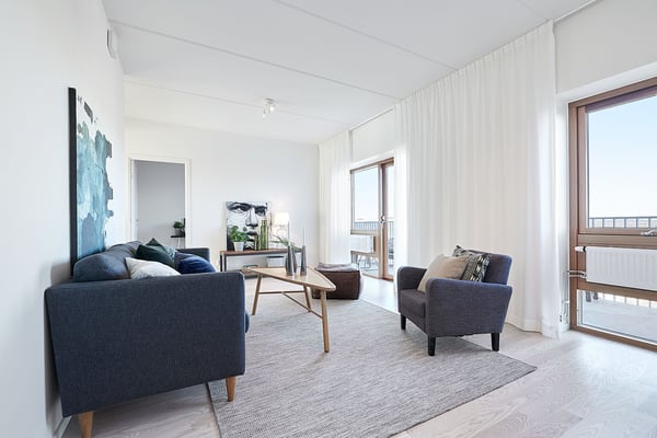 Ljust vardagsrum med mörk soffa, fåtölj, soffbord och stora fönster