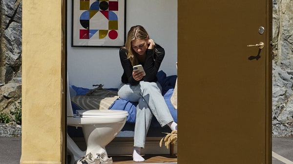 Person som sitter på en säng och använder mobil i ett minihus