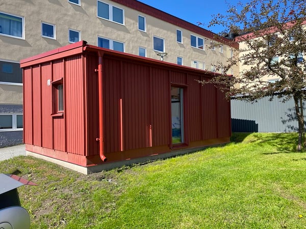 Röd träbyggnad med entré, fönster och bänk utanför