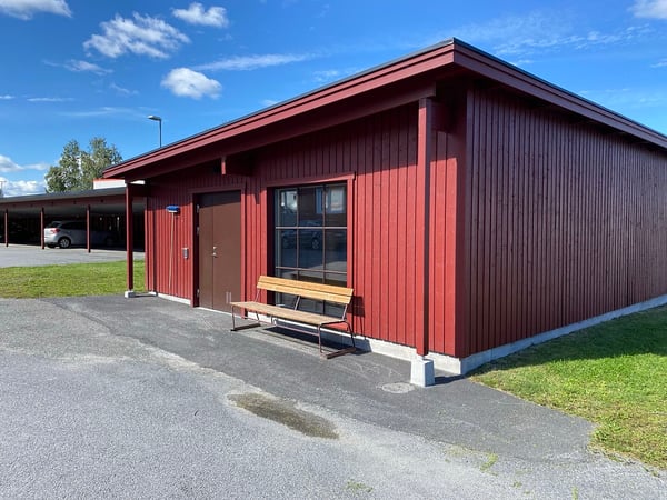 Röd träbyggnad med entré, fönster och bänk utanför