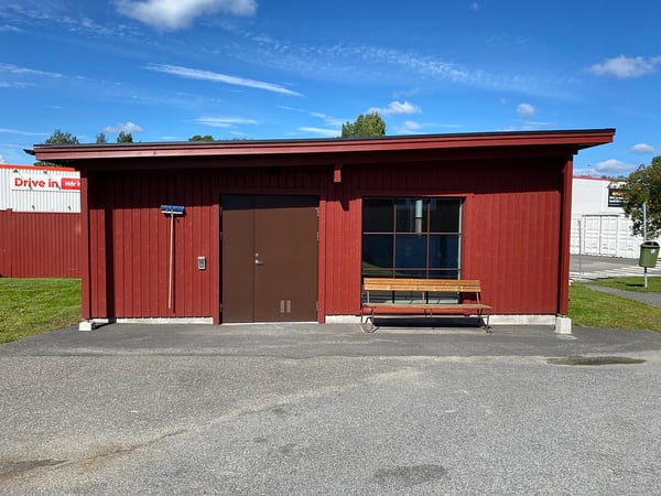 Röd träbyggnad med entré, fönster och bänk utanför