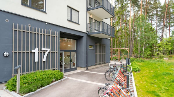 Flerbostadshus med nummer 17, entré och cykelparkering vid grönskande skogsmiljö