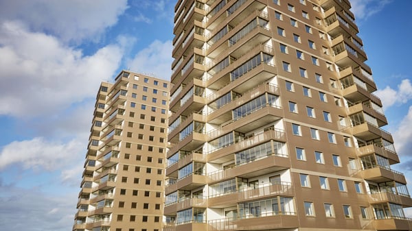 Två moderna bostadshus i beige med balkonger och många fönster mot blå himmel