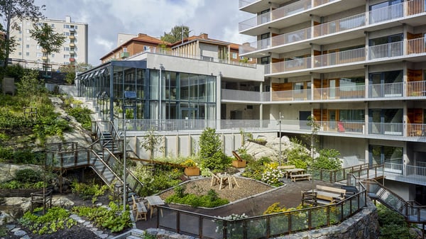Bostadshus med balkonger och en grön innergård med trappor, gångvägar och planteringar