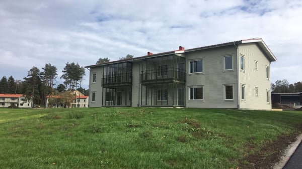 Hus med ljus fasad, glasade balkonger och gräsmatta framför