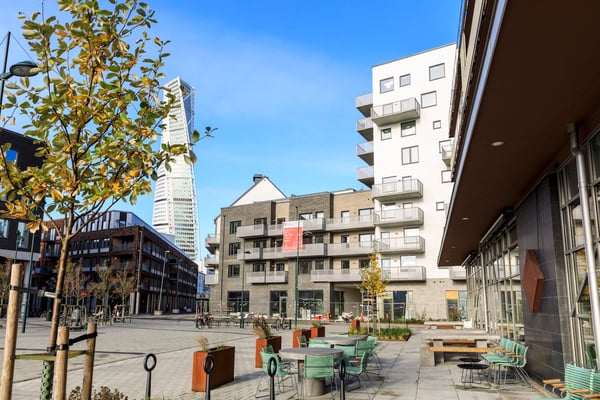 Fastighet i modern bostadsmiljö med innergård, sittplatser och höghus i bakgrunden