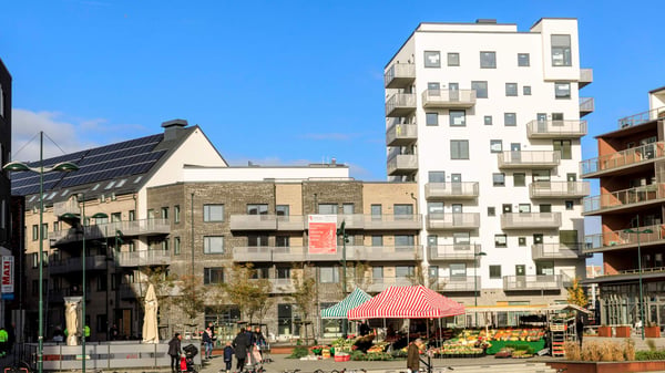 Urbant bostadskvarter med flerfamiljshus, balkonger och en torgyta med marknadsstånd framför