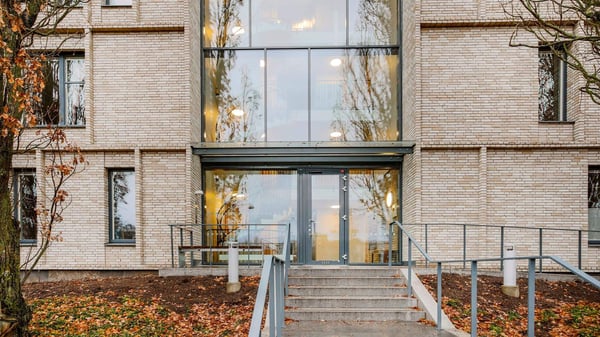 Flerbostadshus i ljus tegel med entré, trappa och stora fönster