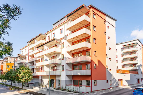 Flerfamiljshus med vita och röda fasader, balkonger och omgivande grönska under en klarblå himmel