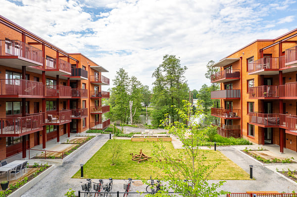 Lägenhetskomplex i modern arkitektur med röda fasader och balkonger, omgivna av grönska och en välskött innergård
