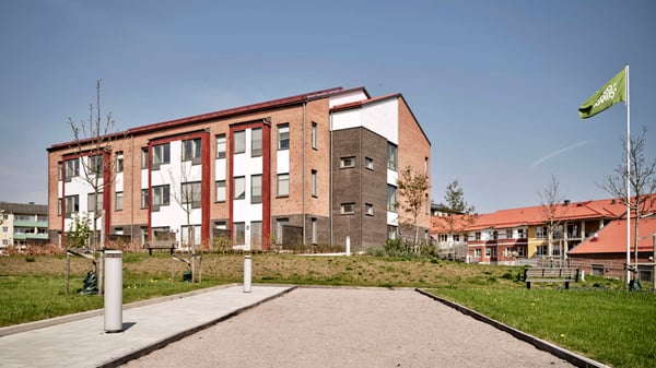 Bostadshus i tegel med grönytor och gångväg framför