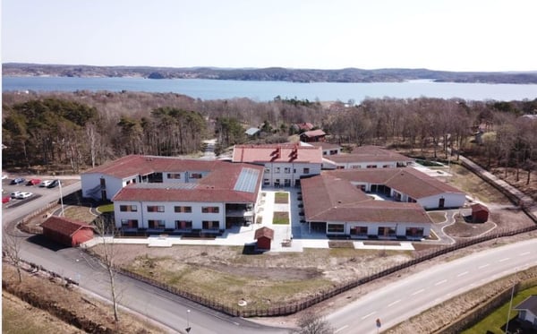 Flygvy över bostadshus med röda tak vid vatten och skog