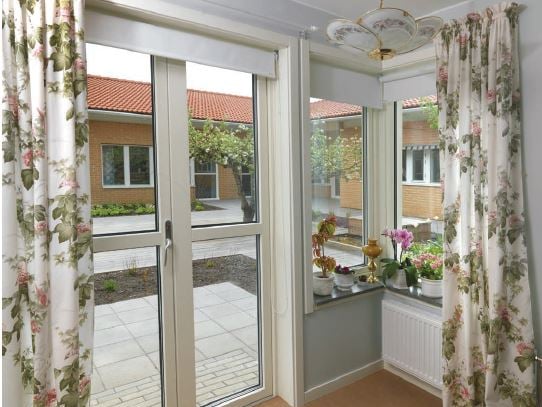 Inglasad uteplats med dörr, stora fönster och blomsterprydda gardiner