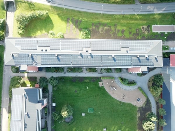 Flygvy över flerbostadshus med solpaneler på taket och grön innergård