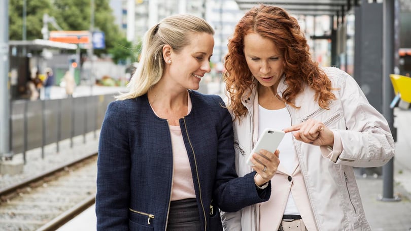 Två kvinnor tittar på telefon på spårvagnsperrong
