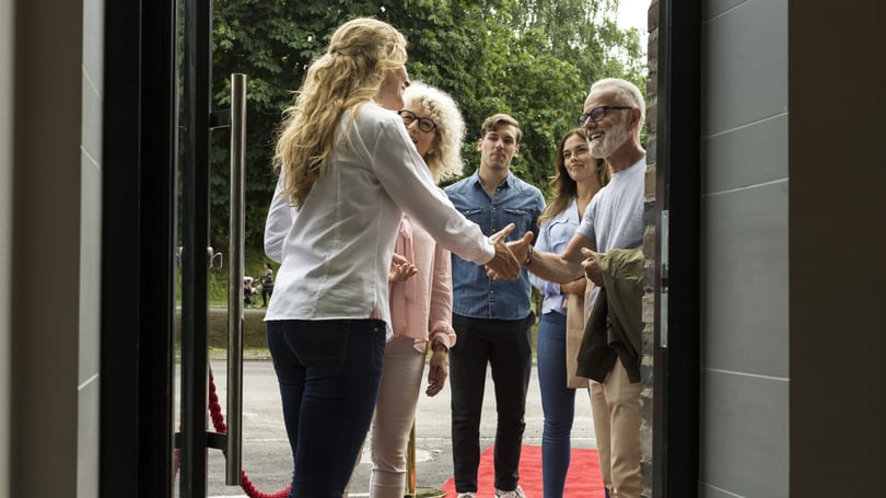 En grupp människor hälsar på varandra vid en dörr, där en röd matta ligger utlagd