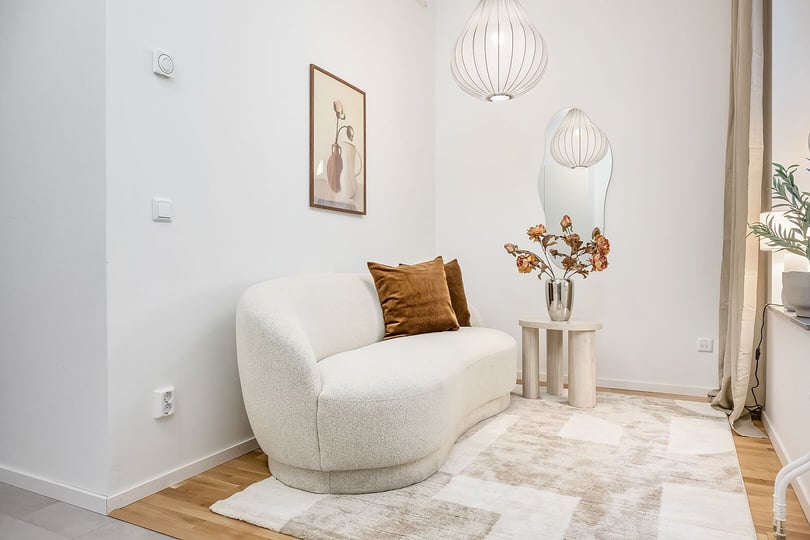 Modern vardagsrum med ljus soffa, bruna kuddar, sidobord med en vas och blommor, väggkonst, och hängande taklampor