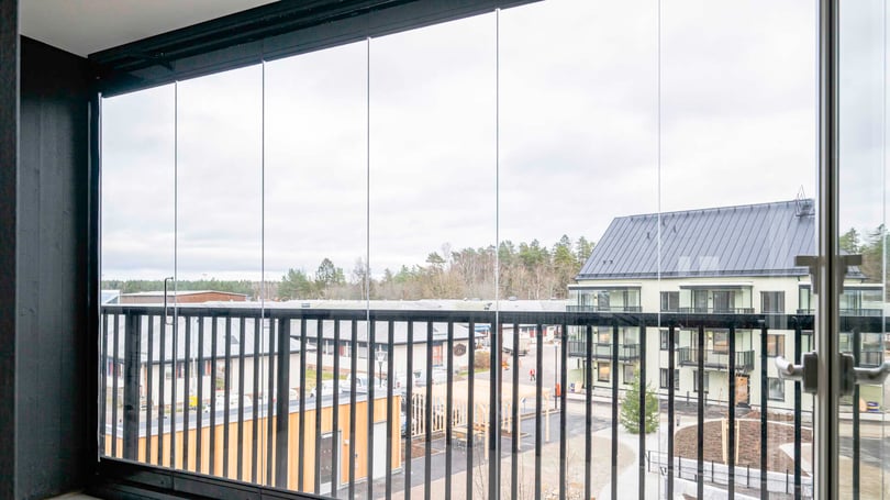 Balkong med glasräcke och utsikt över ett bostadsområde med moderna byggnader och träd i bakgrunden