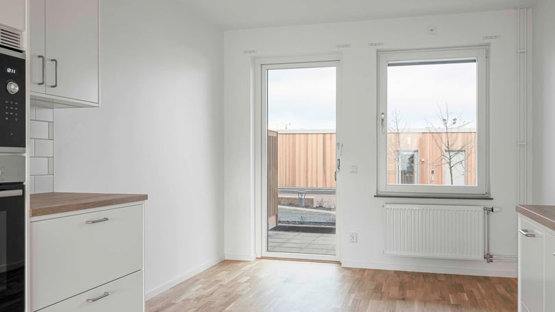 Modernt kök med vita skåp, trägolv och en glasdörr som leder ut till en träbeklädd uteplats