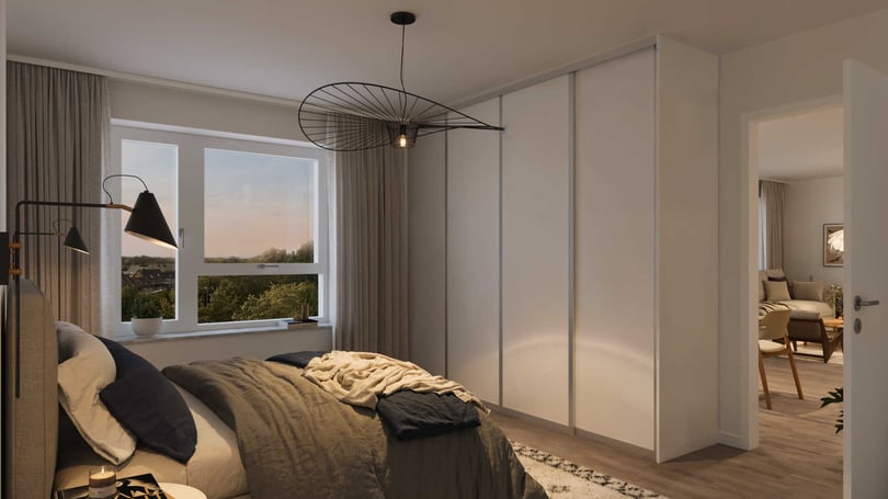 Sovrum med stor säng, krämfärgade gardiner, en modern taklampa och vit garderob, med utsikt över natur genom fönstret. En öppen dörr leder till ett annat rum med fåtölj