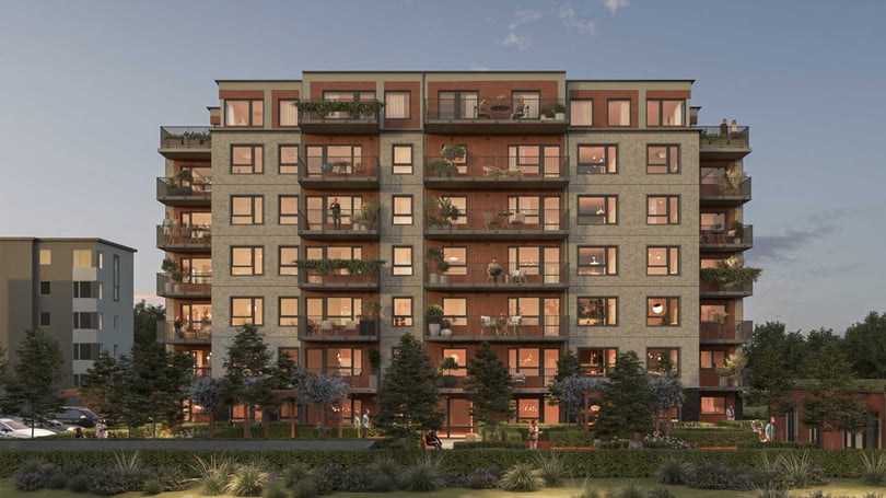 Flerfamiljshus med flera våningar, balkonger och stora fönster, omgiven av grönska och med en blå himmel i bakgrunden