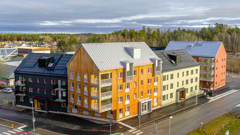 Nybyggd flerfamiljsfastighet med modern design, inkluderande fasader i trä, puts och metall, belägen vid en korsning i ett bostadsområde