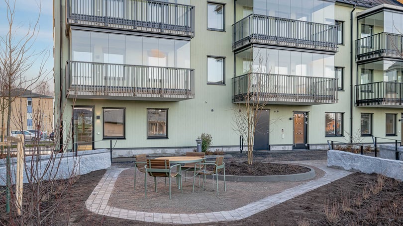 Flerbostadshus med grön fasad, glasbalkonger och en nyanlagd innergård med sittmöbler och stensatta gångar