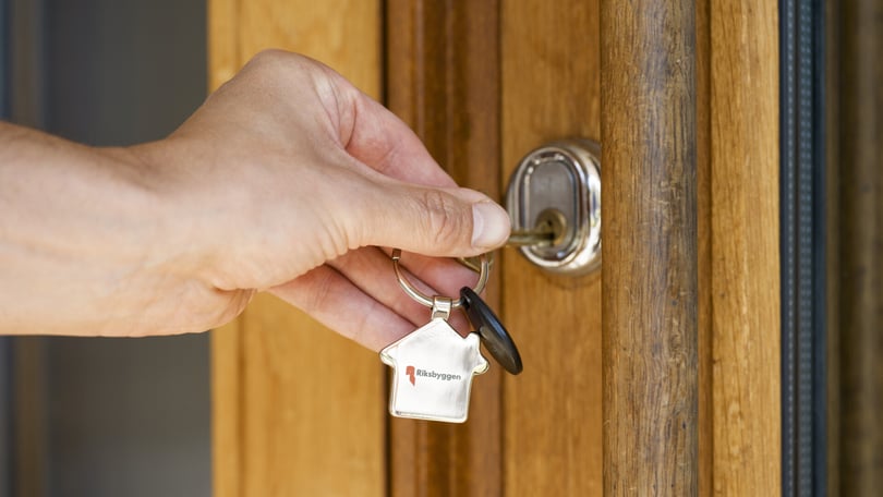 Hand som håller en nyckelknippa med en nyckel insatt i ett dörrlås av trä
