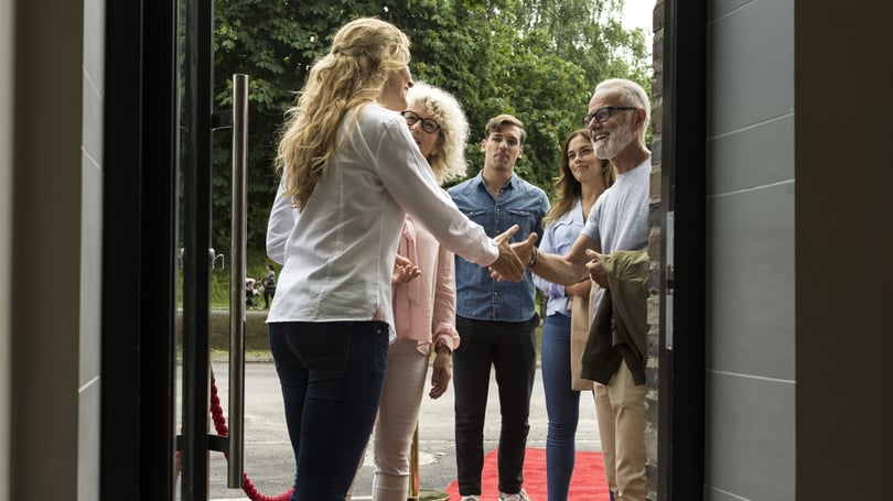 En grupp människor hälsar på varandra vid en dörr, där en röd matta ligger utlagd