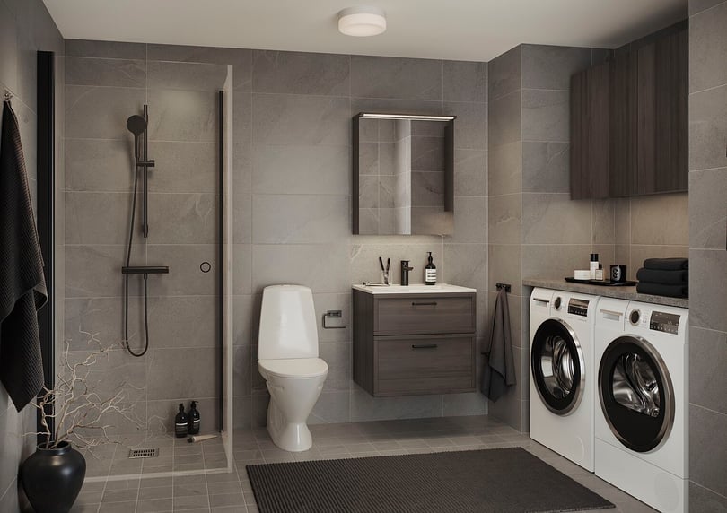 Modernt badrum med duschhörna, toalett, handfat med spegelskåp och tvättmaskin samt torktumlare på rad. Grå klinker och mörka trädetaljer