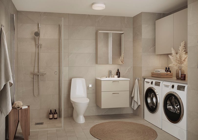 Modernt badrum med beige kakel, dusch med glasvägg, toalett, tvättmaskin och torktumlare, samt kommod och spegel. Dekorationer inkluderar handdukar, tvålflaskor och torkade växter