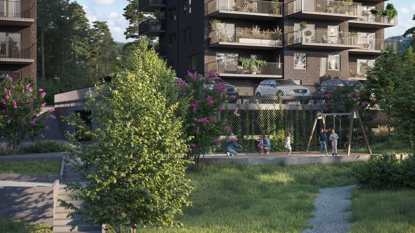 Bostadshus med balkonger fyllda med växter, omgivna av grönska och blommor. Främre delen av bilden visar en lekplats med barn och en gångstig