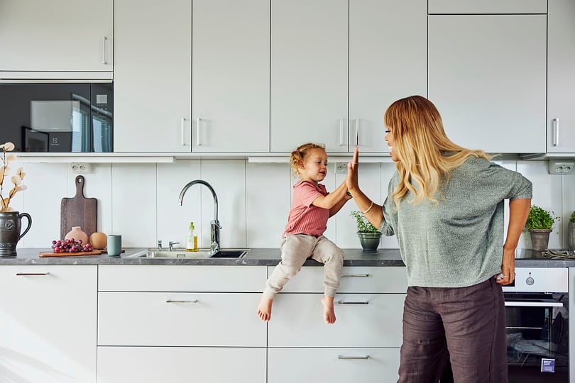 Kvinna och barn i ett modernt kök, där barnet sitter på köksbänken och ger kvinnan en high-five