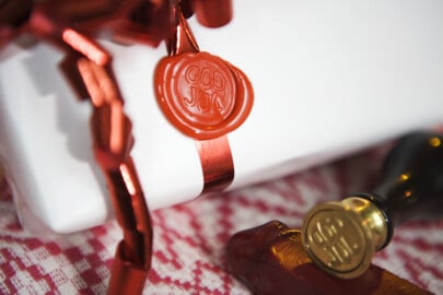 Vitt paket inslaget med röd presentband och sigillstämpel, liggande på ett rött och vitt mönstrat tyg