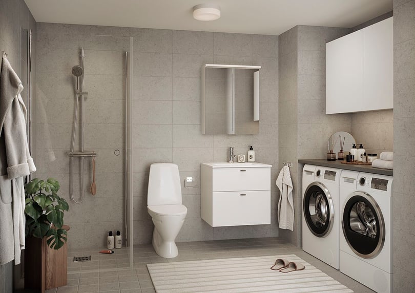 Badrum med grå kakelväggar, dusch med glasvägg, toalett, vit tvättställskåp, spegel, tvättmaskiner och torktumlare, samt en grön växt och vita handdukar