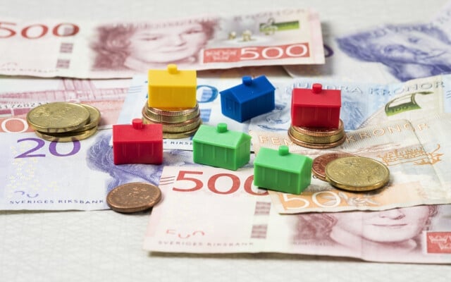 Svenska sedlar och mynt med små färgglada husmodeller placerade ovanpå