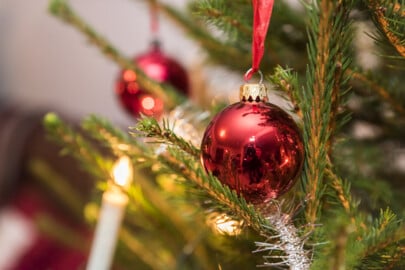 Röd julgranskula hänger i en gran med gröna grenar, omgiven av ljus och dekorationer